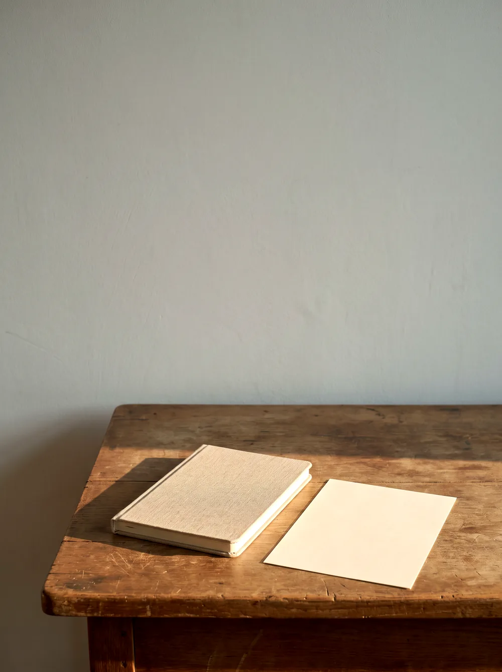 Un plan de travail en bois presque vide dans la lumière du soir : un carnet fermé et une feuille.