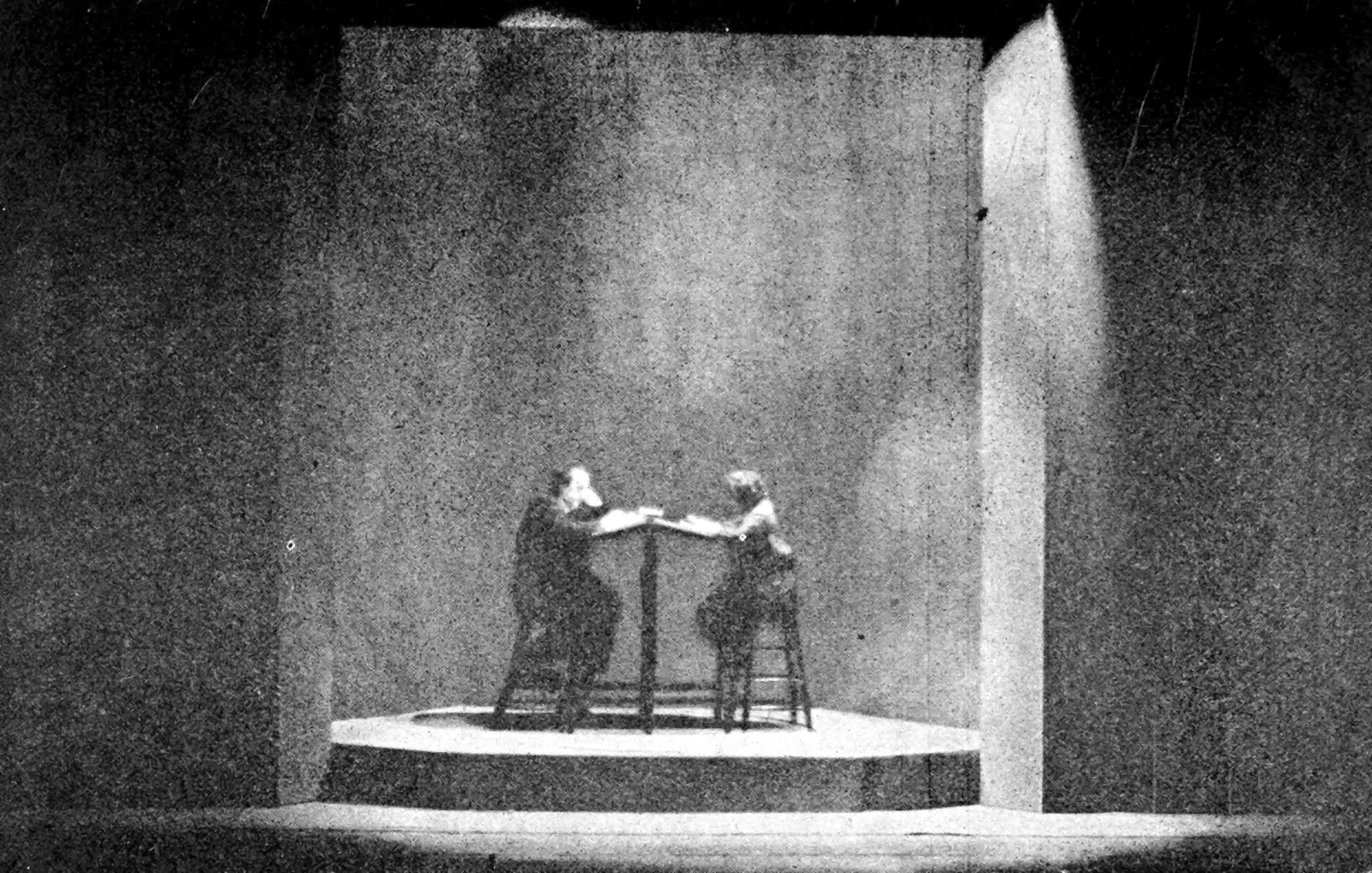 Décor de théâtre de 1923 : deux comptables minuscules à un pupitre, au pied d'un mur gris immense.