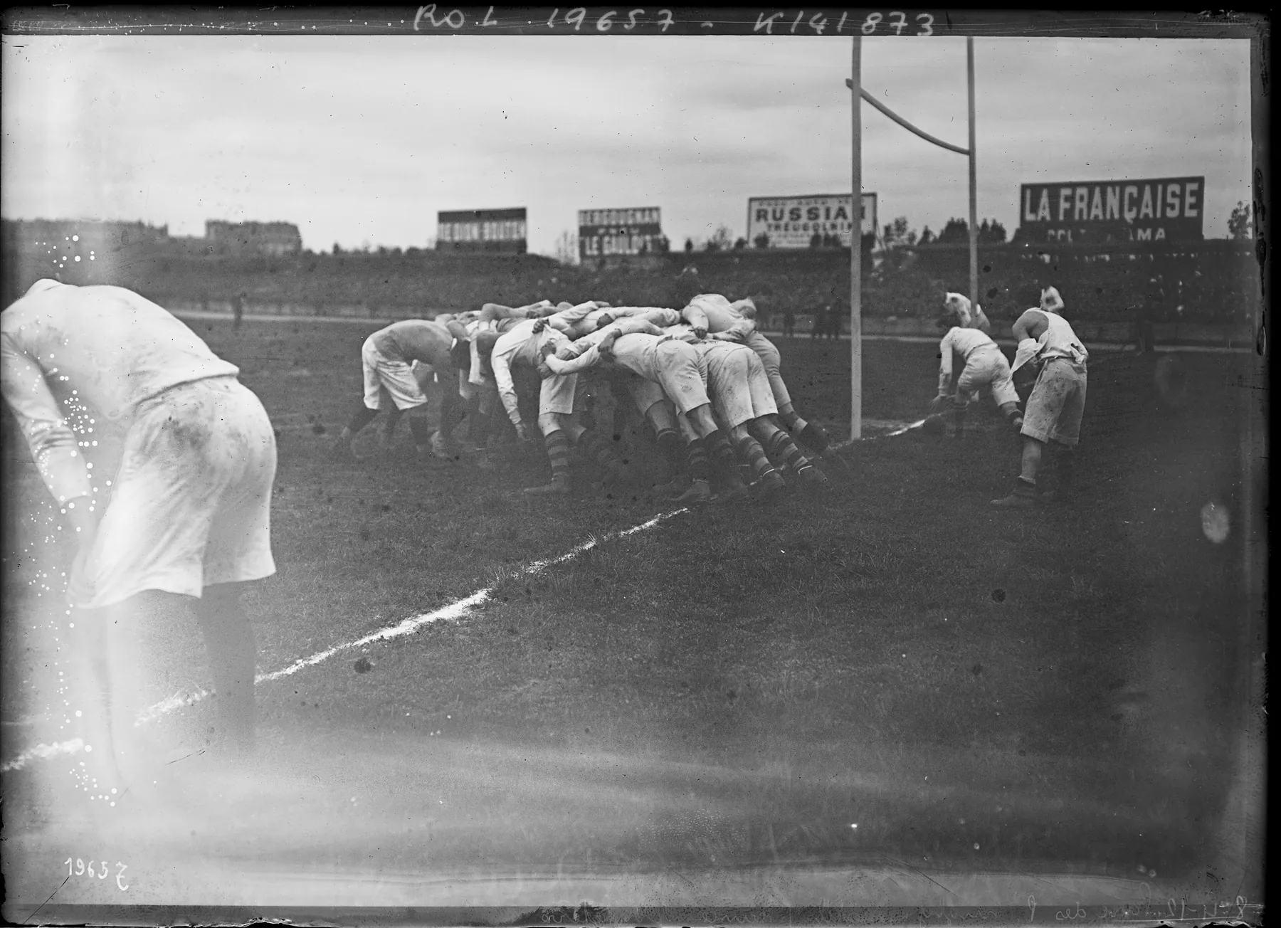 Une mêlée de rugby au Parc des Princes en 1912 ; au fond du stade, des panneaux publicitaires